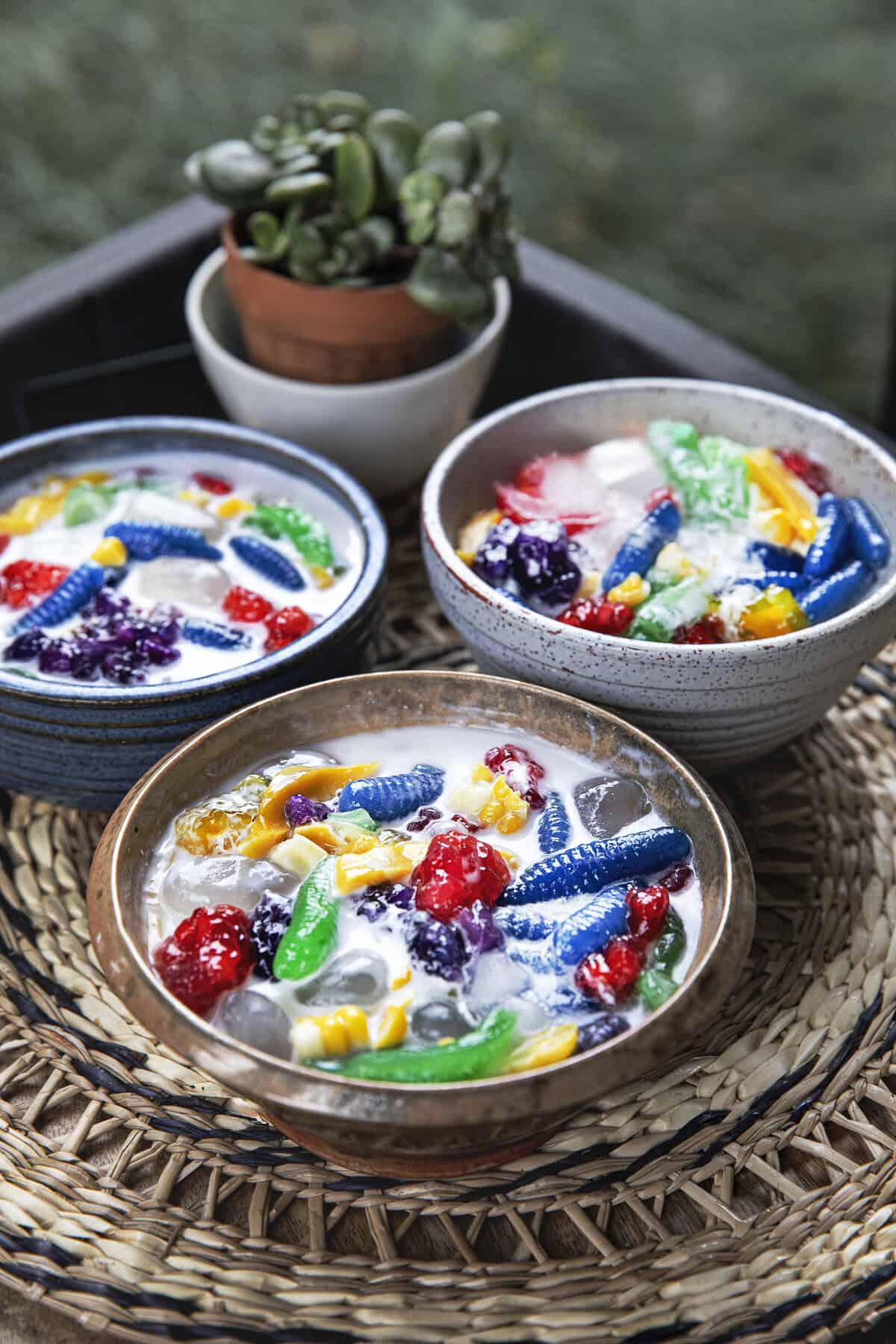 3 bowls of Ruam Mit dessert with colorful chewy tapioca pieces, jackfruit, sweet corn, coconut milk, and crushed ice.