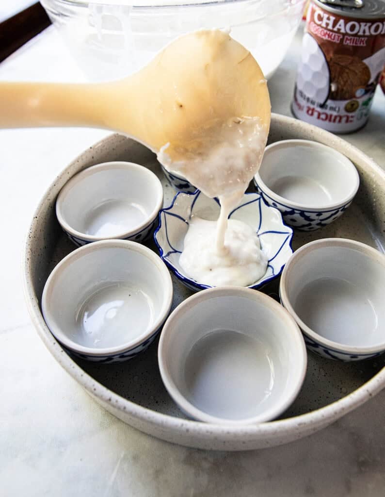 Filling cups with Khanom Kluay batter spooned into small Thai ceramic cups.