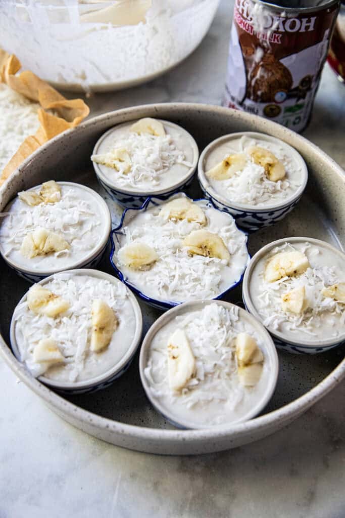 Khanom Kluay topped with banana slices and shredded coconut before steaming.