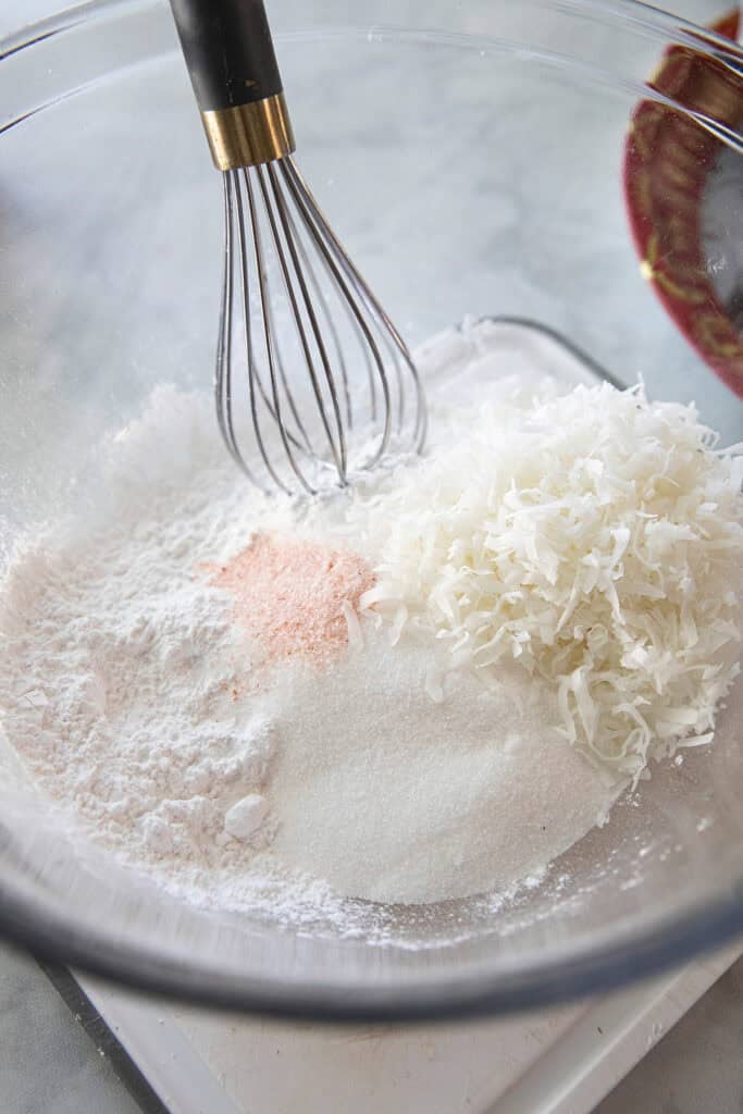 Dry ingredients for khanom Klouy with Rice flour, tapioca flour, sugar, salt and shredded coconut in a mixing bowl.