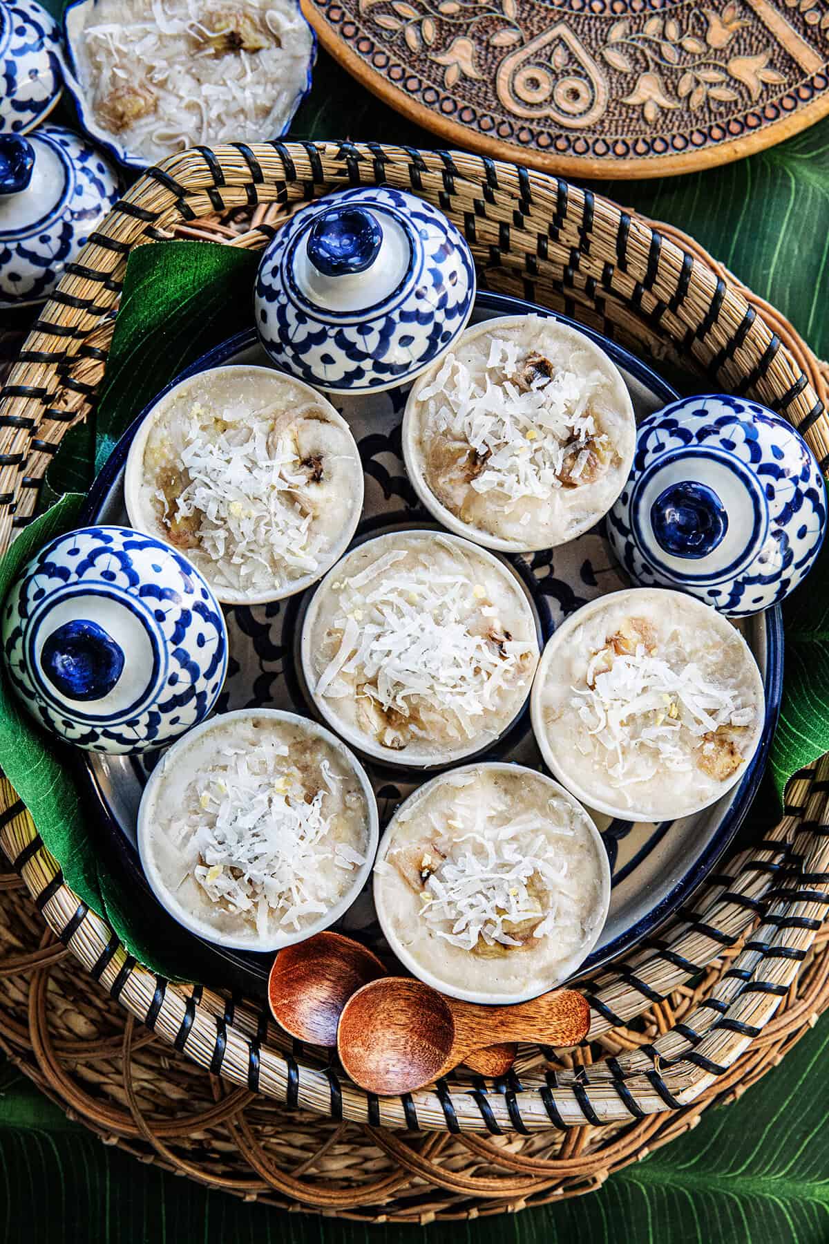 Khanom Kluay Thai steamed banana dessert topped with shredded coconut in round cups in a basket.