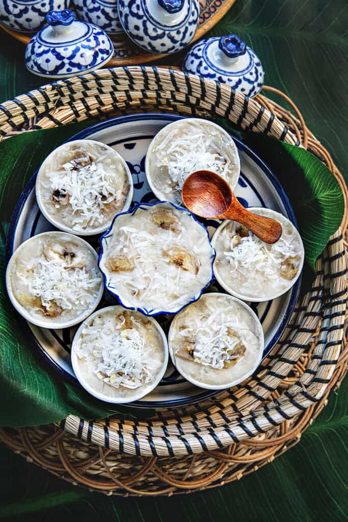 Khanom Kluay Thai steamed banana dessert in small cups in a bamboo basket.